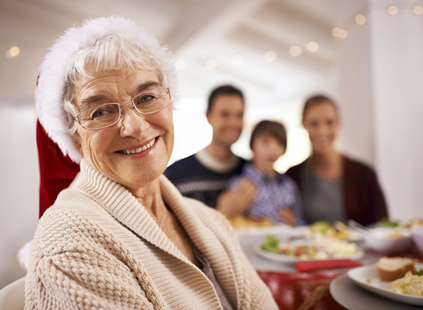 A senior woman smiles contentedly at the camera at a family holiday dinner.