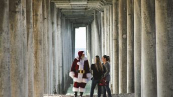 Two women meet Santa Clause under the dock at the beach for a CovidSafe Holiday