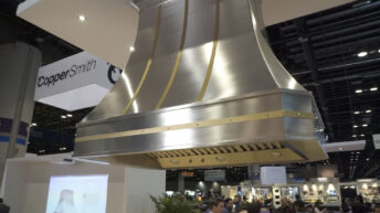 World Coppersmith Custom Range hoods, sinks, tables and fire pits, image of large brushed nickel range hood with gold trim in large Coppersmith showroom