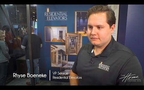 Residential Elevators create Accessible Home, elevator showroom with dark blue walls, photos of construction, man in black polo and short dark hair. Text: Rhyse Boeneke, VP Service, Residential Elevators