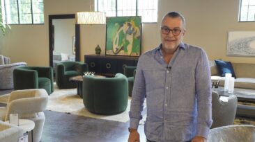 Tomlinson Co. & Scott Carpenter design furniture, tall man with hair pulled back and glasses in grey button down shirt, in furniture showroom with green and off white swivel chairs and decor