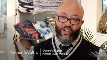 Norman Wyatt Home Lifestyle Collection with StyleCraft showroom, black man with dark beard and black-rimmed glasses in black and white vest, colorful throw pillows in background. Text: Norman Wyatt, Jr., Owner & Designer, Norman Wyatt Home, LLC