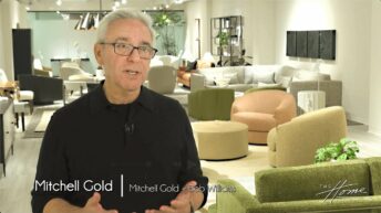 man with white hair and black shirt in Mitchell Gold + Bob Williams furniture showroom, modern tan swivel chairs. Text: Mitchell Gold, Mitchell Gold + Bob Williams
