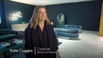 Caracole Luxury Furniture showroom with dark blue walls and blue modern couches, woman with long blond hair wearing black shirt, decorative modern lighting with globes. Text: Katie Coggins, Caracole director of merchandising
