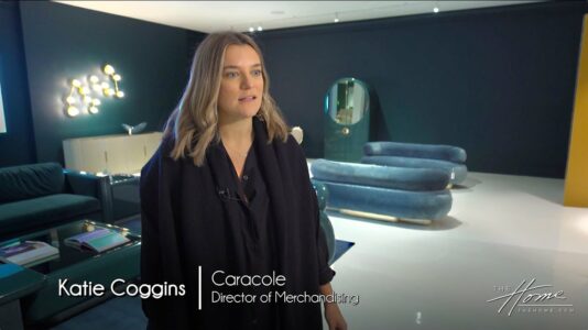 Caracole Luxury Furniture showroom with dark blue walls and blue modern couches, woman with long blond hair wearing black shirt, decorative modern lighting with globes. Text: Katie Coggins, Caracole director of merchandising