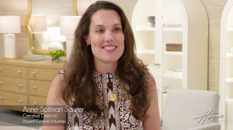 Image: smiling woman with long brown hair wearing brown and white dress, in a furniture showroom