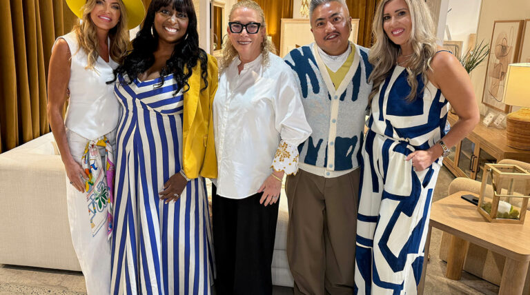 Image: group of 4 women and one man, all wearing white and blue outfits in a furniture showroom