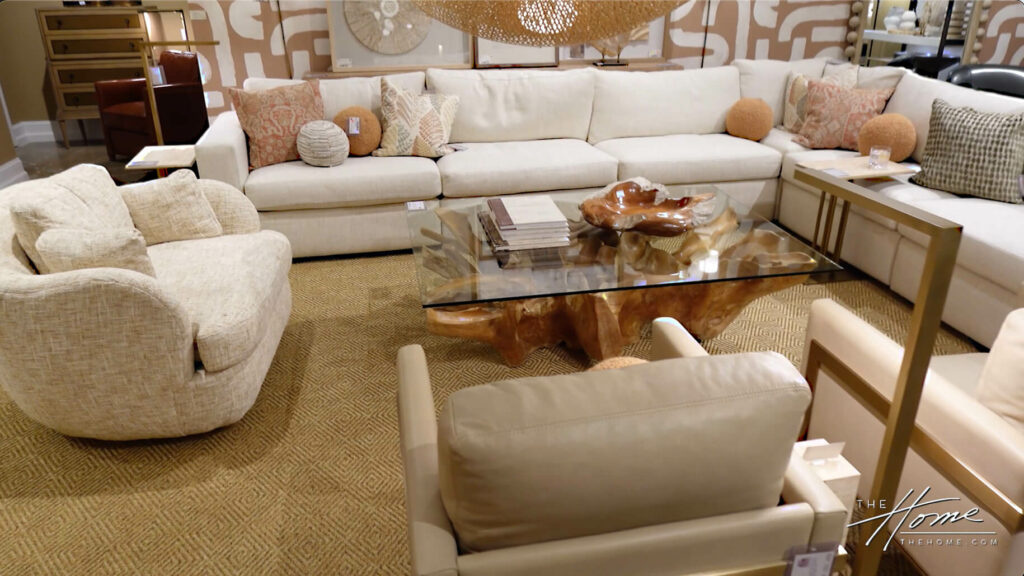Image: off white modular sofa with peach pillows in various shapes, tan side chairs, jute carpet, glass coffee table with tree root wooden base