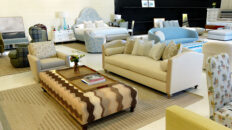 Image: Design Theory showroom with brown striped upholstered coffee table, beige sofa, tan carpet, upholstered blue headboard