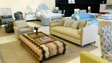 Image: Design Theory showroom with brown striped upholstered coffee table, beige sofa, tan carpet, upholstered blue headboard