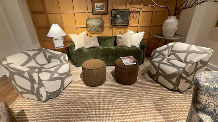 Image: Norwalk Furniture showroom with velvet green modern couch, cream pillows, 2 abstract fabric swivel chairs, tan rug, brown pouf ottomans