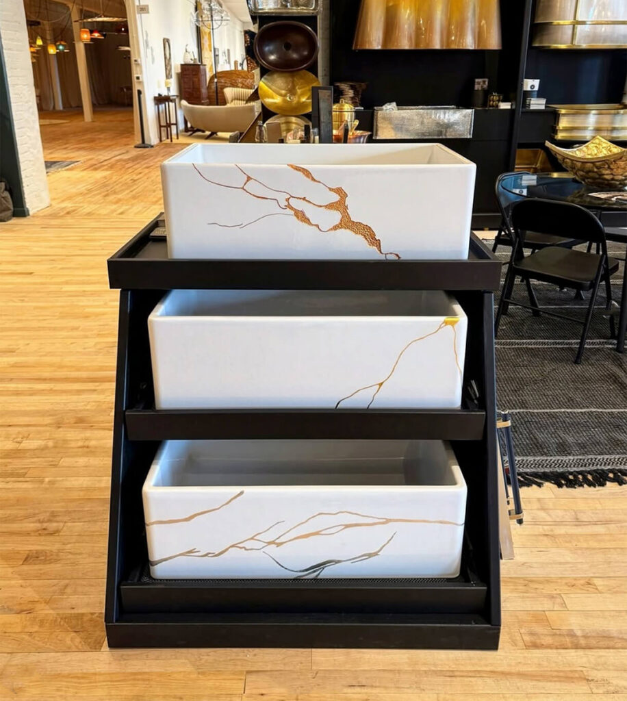 Image: 3 white Kintsugi freckly sinks with etched metal cracks in gold, silver, copper on black wood shelving in Thompson Traders showroom