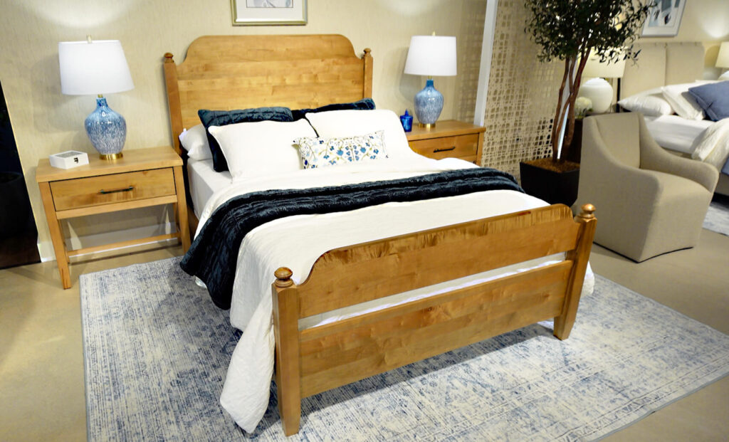 Warm honey colored wood bed with poster knobs, white and blue bedding in furniture showroom