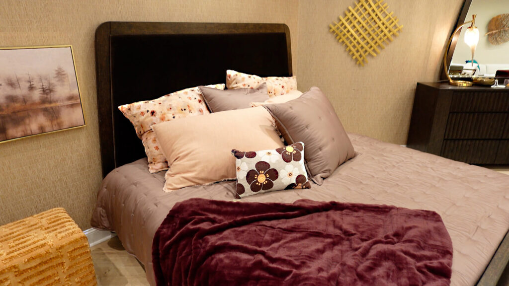 Jessica Simpson Home Collection upholstered bed headboard with pink and burgundy pillows and dark wood dresser by Steve Silver Furniture
