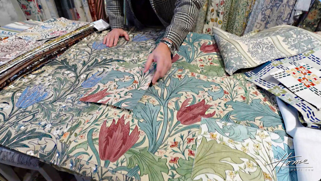 Arts & Crafts John Henry Dearle design Lent Lily fabric pattern in blue, rust, green on cream background, sales manager Paul Morrison 
pointing to details in the fabric