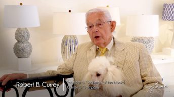 older man with white hair and tan striped seersucker jacket holding white poodle, in Currey & Company showroom, ceramic lamps in background