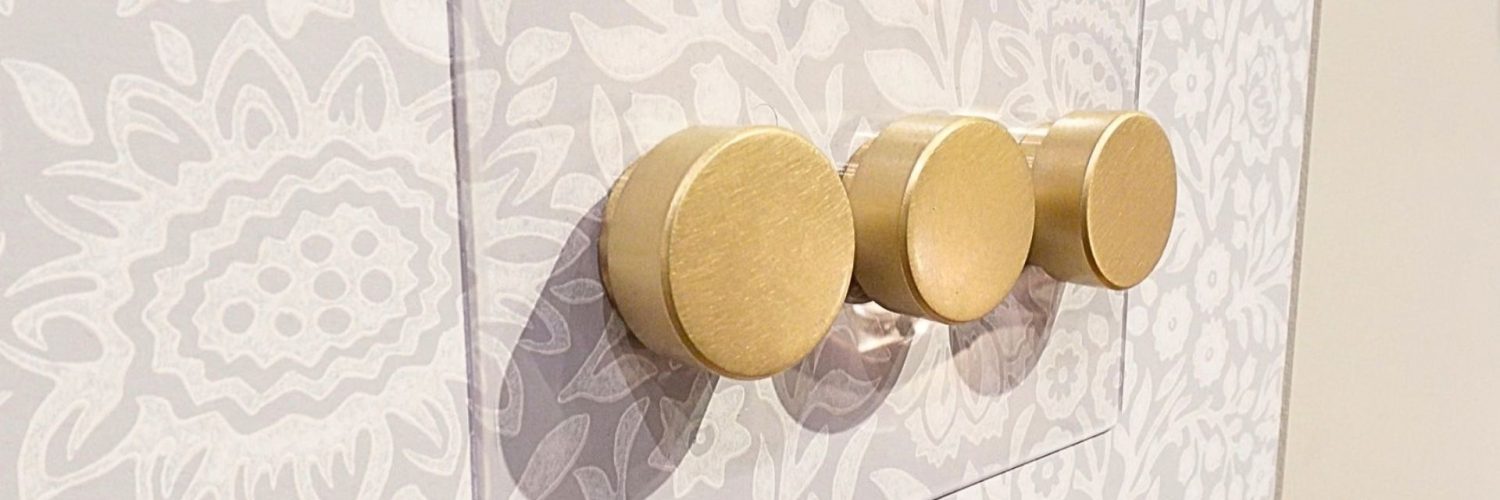 antique brass light switches and a clear backplate on taupe pattern wallpaper
