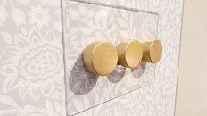 antique brass light switches and a clear backplate on taupe pattern wallpaper