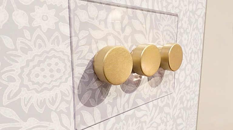 antique brass light switches and a clear backplate on taupe pattern wallpaper