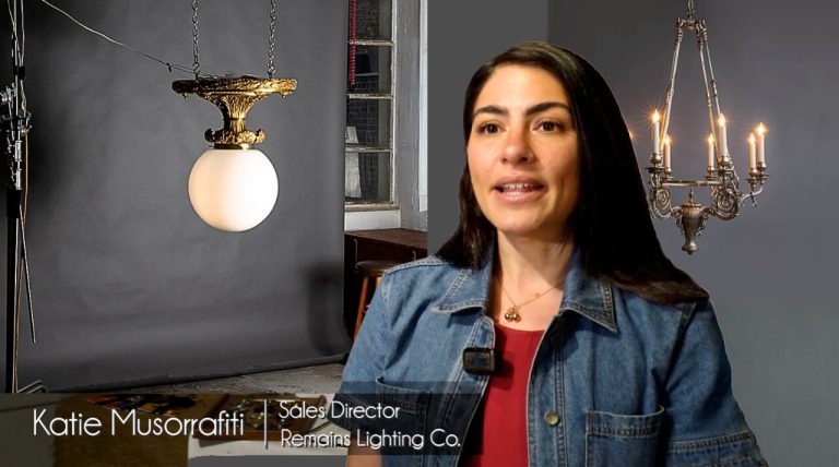 woman with dark hair in dark studio with antique brass globe light and vintage pewter chandelier, text says Katie Musorafiti ,Sales Director Remains lighting Co.